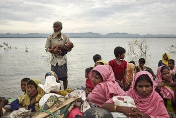 一名罗兴亚难民怀抱一名婴儿，搭乘临时制成的小船，渡过缅甸与孟加拉国的界河纳夫河。