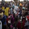 South Sudanese people, including many children and women, are gathered in a crowded outdoor setting in Unity State.