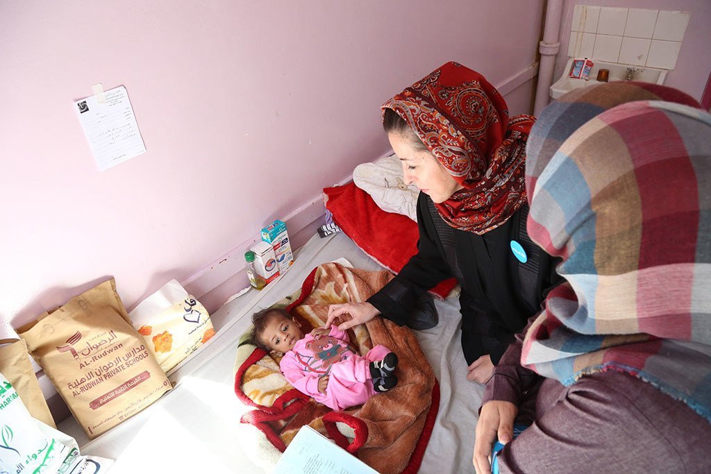 Un trabajador de UNICEF en Yemen examina a un bebé desnutrido en una cama de hospital mientras su madre observa.