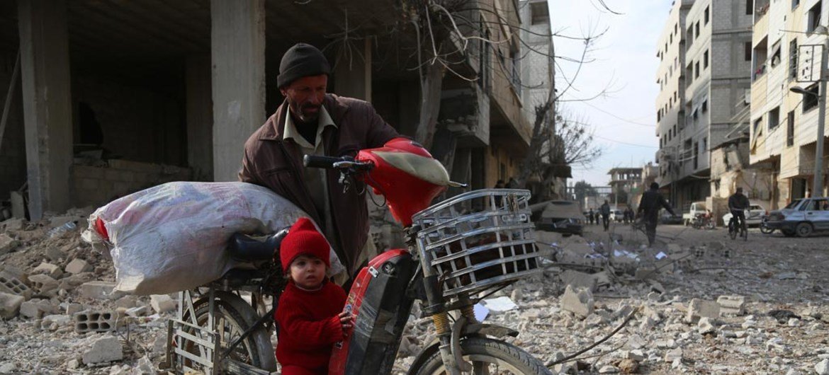 Ru’a, 18 months, rides on her grandfather’s motorbike as he drags it across Mesraba in East Ghouta, Syria.