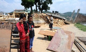 Two girls speak to a psychologist using a mobile phone in rural sindhupalchowk, Nepal. In the background, a house lies in ruin, destroyed by the devastating 2015 earthquakes in country.