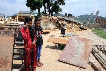 Two girls speak to a psychologist using a mobile phone in rural sindhupalchowk, Nepal. In the background, a house lies in ruin, destroyed by the devastating 2015 earthquakes in country.
