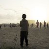 A young child looks on as older boys play football next to a camp for internally displaced persons (IDP) in Mogadishu, Somalia.