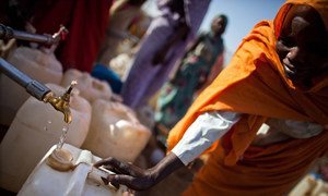 En la fotografía, una mujer de cincuenta años llena su bidón de agua en el campamento para desplazados internos de Abu Shouk, en el norte de Darfur.