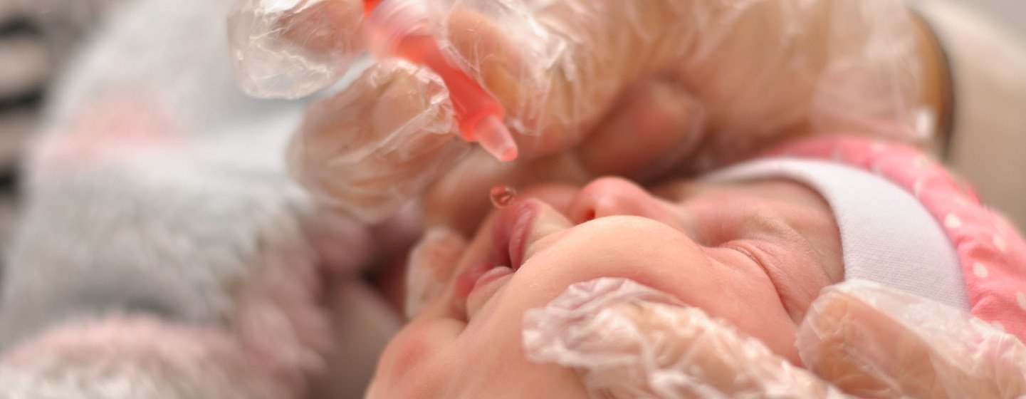 Uma mão enluvada administra uma vacina oral a um recém-nascido.