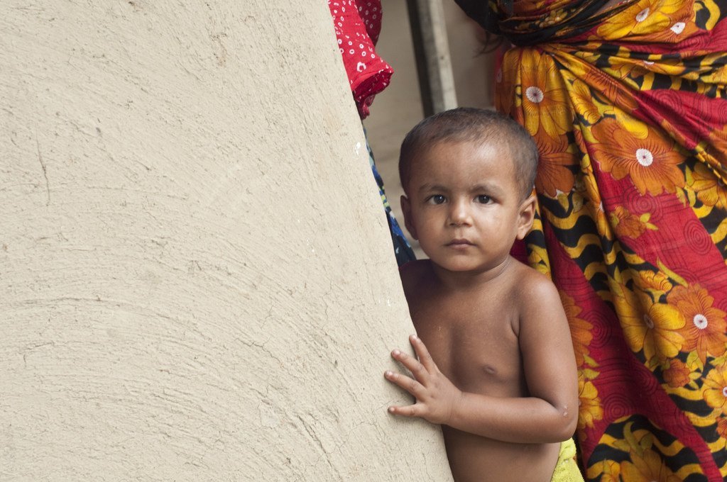 Un enfant se tenant derrière un mur dans la maison de ses parents en zone rurale, au Bangladesh.