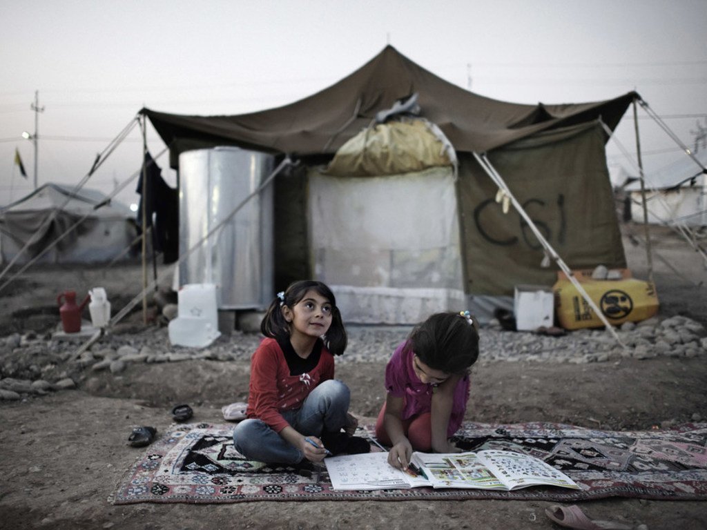 Seated on a rug atop the dirt ground, two girls complete homework outside their tent home, in the Kawergosk camp for Syrian refugees, west of Erbil, Iraq.