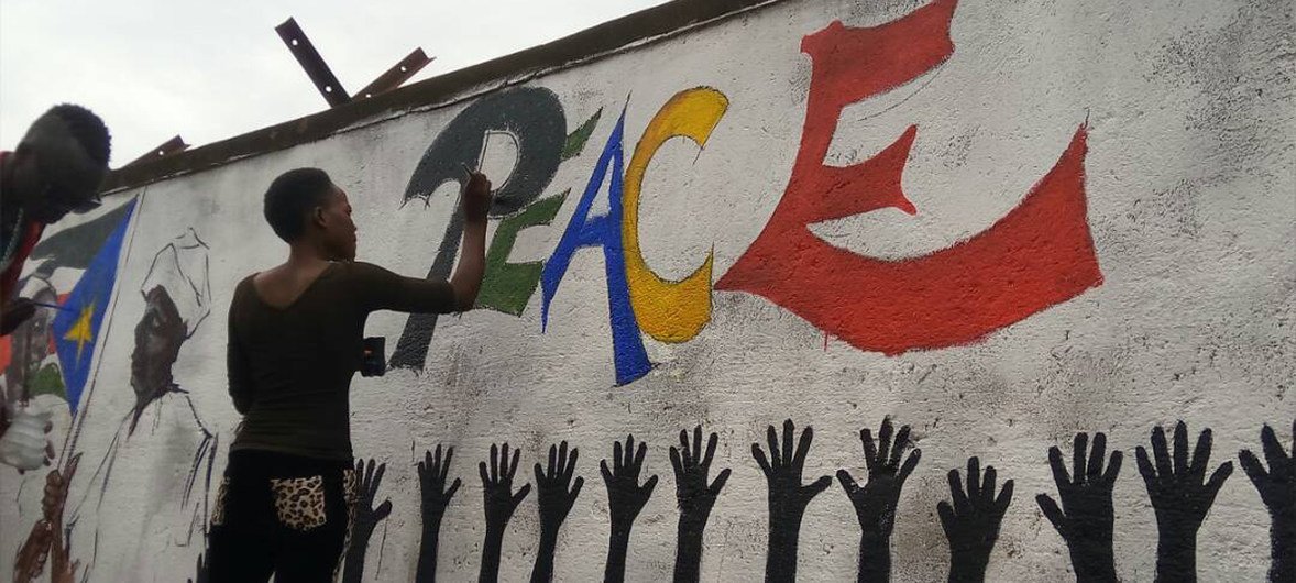 Une femme peint un message de paix sur un mur à Yei, au Soudan du Sud.  Un groupe de peintres mène un effort collectif qui vise a affiché des messages sur la paix et l'harmonie dans de nombreux endroits de la ville.