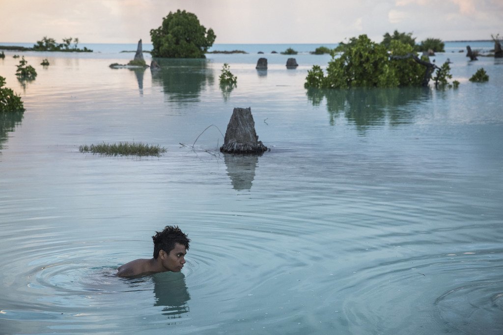 شاب من جمهورية كيريباس بالمحيط الهادئ يسبح في منطقة غمرتها المياه. جزر المحيط الهادئ من أشد البلدان تأثرا بتغير المناخ.