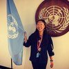 Якутская активистка Мария Ковнер улыбается, держа в руках флаг United Nations на фоне эмблемы ООН .
