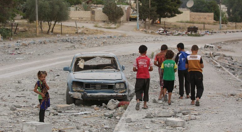En Al Tabqa, Siria, un grupo de niños pasan al lado de un coche destruido. Más de 850.000 niños siguen viviendo en zonas sitiadas de Siria.
