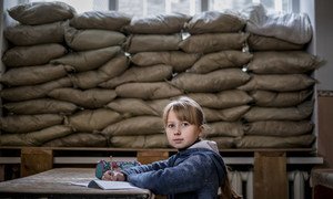 A child sits in a classroom in Ukraine with sandbags reinforcing the window to protect against shrapnel and bullets.