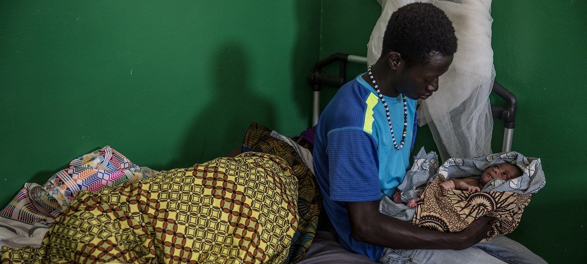Um jovem pai na Guiné-Bissau com seu bebê recém-nascido.