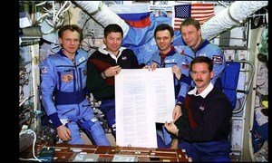 La tripulación del segundo transbordador Mir de la misión de acoplamiento sujeta una copia del Tratado sobre el Espacio Ultraterrestre, que firmaron en órbita, para celebrar el quincuagésimo aniversario de las Naciones Unidas.
