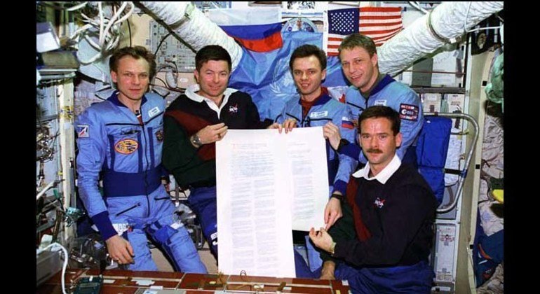 The crew of the second Shuttle-Mir Docking mission hold a copy of the Outer Space Treaty that they signed in orbit to celebrate the fiftieth anniversary of the United Nations.