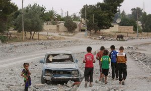穿着红色T恤的12岁叙利亚儿童哈桑（左二）与朋友们走过一辆被炸毁的汽车。哈桑一家已经两次为躲避暴力而逃离家园，使得他被迫从小学三年级辍学。