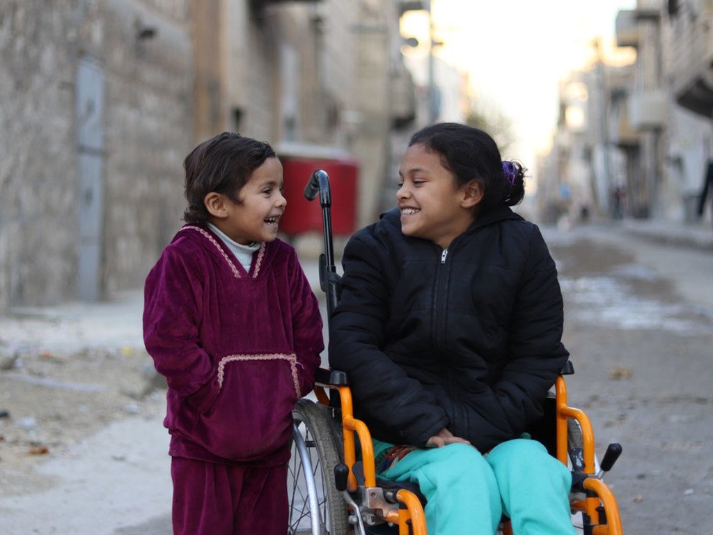 Una niña siria que perdió el movimiento de sus piernas tras un bombardeo, comparte con su hermana pequeña en Aleppo. 