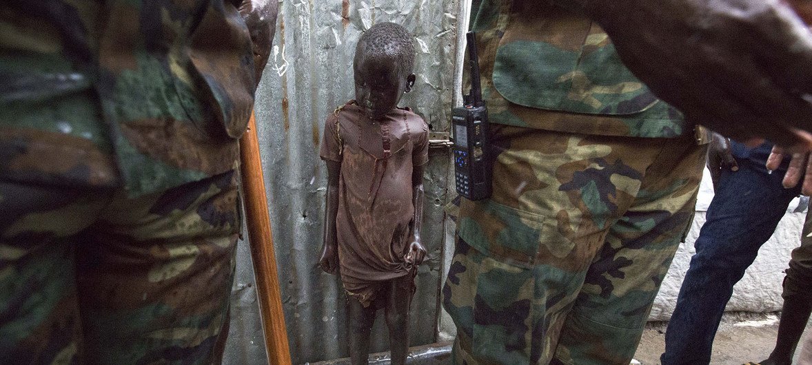 在南苏丹里尔的联合国南苏丹特派团基地附近的临时营地,一名儿童站在来自加纳的维和人员后面。约有2000名平民因最近的冲突在营地中避难。