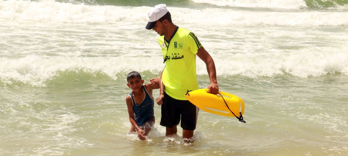 A young man working as a lifeguard helps a child out of the water on a Gaza beach.