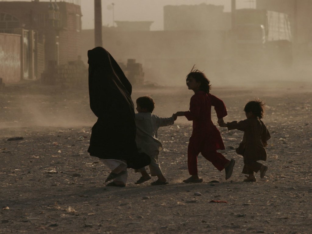 A woman along with her children runs across a dusty street in Herat, western Afghanistan. Civilians across the country continue to bear the brunt of the conflict.