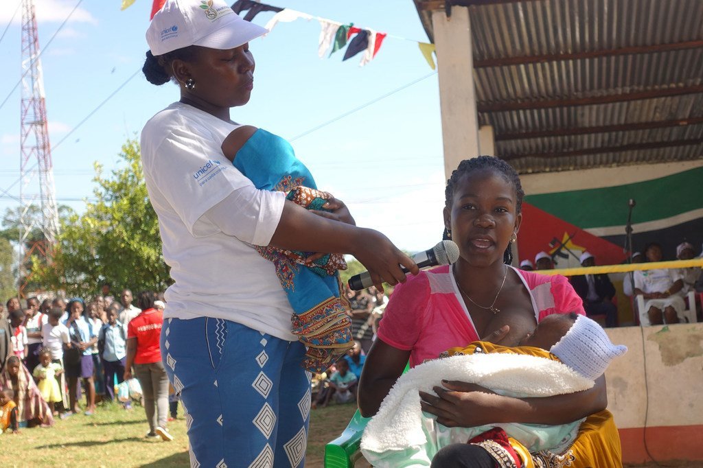 Balozi wa UNICEF Neyma akizungumza katika hafla ya hadhara nchini Msumbiji, huku mwanamke akimnyonyesha mtoto wake karibu.