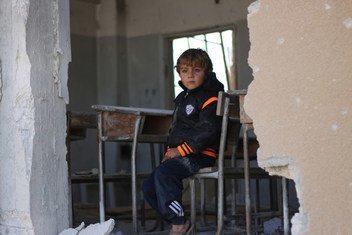 2016年，叙利亚伊德利卜，一名男孩坐在被战火摧毁的教室课桌前。