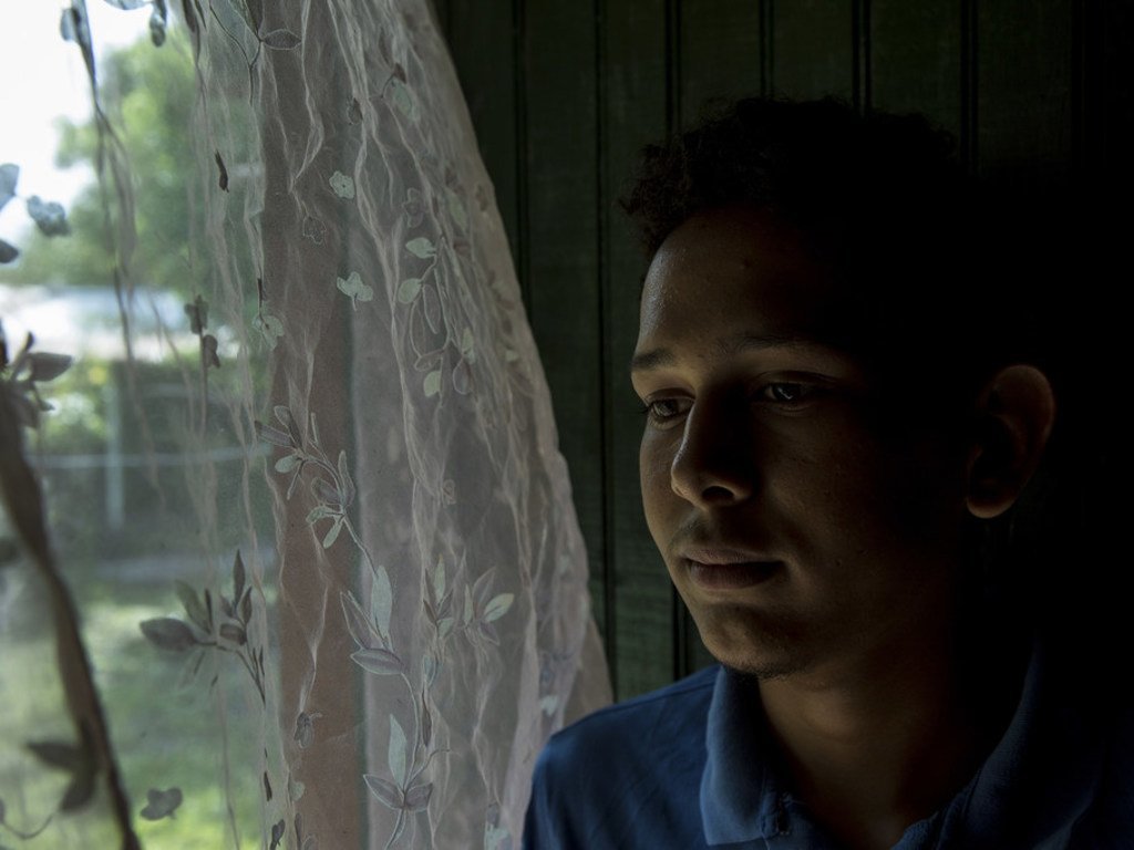 Victor Fernando, 17 ans, se tient près de la fenêtre de son domicile de Villanueva, au Honduras. Il a été victime d'intimidation à l'école concernant son orientation sexuelle. Depuis que l'intimidation a commencé, ses notes ont chuté.