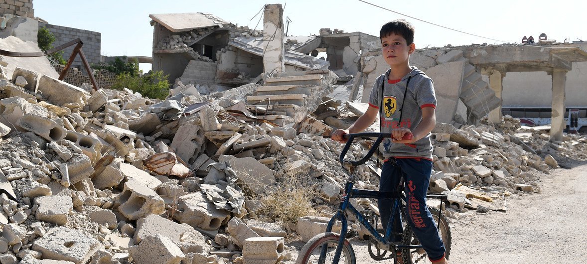 一个小男孩骑着自行车穿过杜马的残垣断壁。