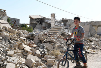 一个小男孩骑着自行车穿过杜马的残垣断壁。