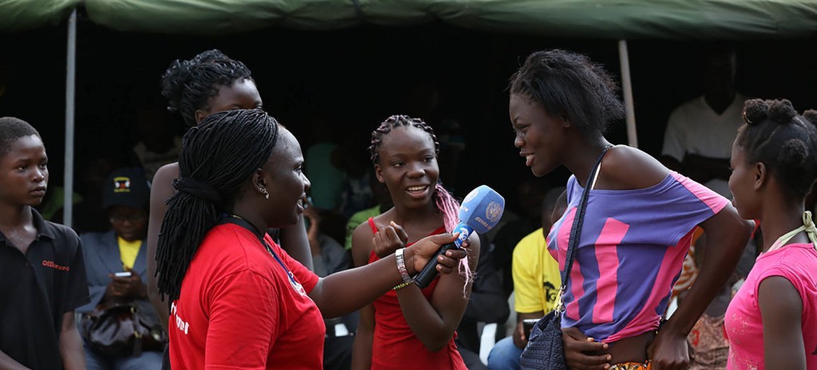 Uma mulher de camisa vermelha entrevista uma jovem com um microfone em um evento ao ar livre organizado pela Guira-FM, uma estação de rádio da ONU que promove a paz e a reconciliação na República Centro-Africana.