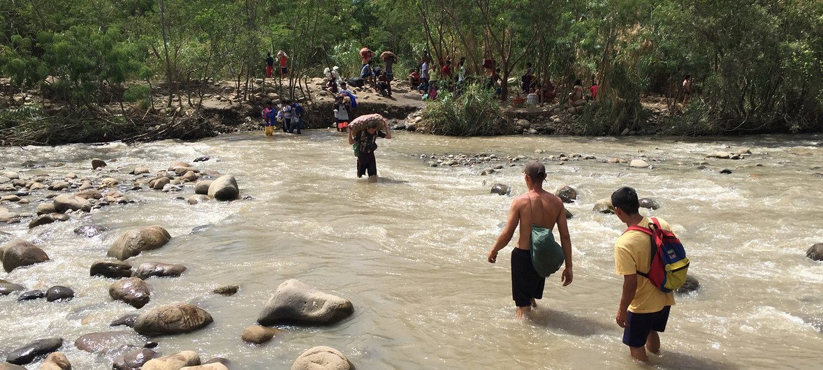 Migrantes Venezuelanos cruzando o rio Trocha, na fronteira da Colombia com a Venezuela.  