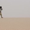 رجل يمشي حافي القدمين على كثيب رملي في منظر طبيعي صحراوي.