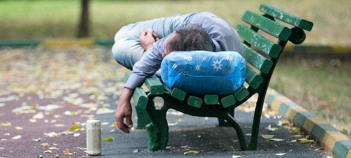 Un hombre ebrio duerme en la banca de un parque.