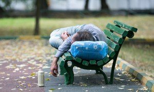 Un hombre ebrio duerme en la banca de un parque.