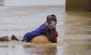 A mother and child attempt to escape the flood water in Niger State, Nigeria, following torrential rains which have hit the region since mid-July 2018. 