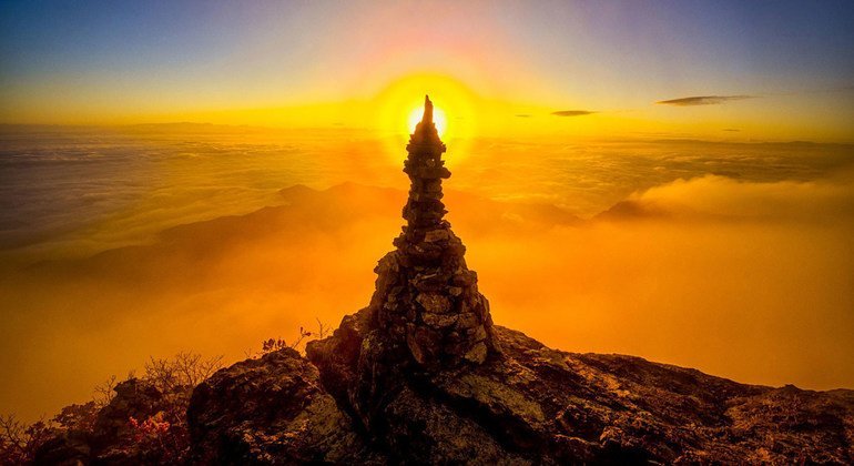 Башня из камней на фоне солнечного гало на рассвете. Гора Кимсо, Республика Корея. 