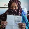 Une femme afghane âgée, coiffée d'un foulard bordeaux, brandit sa carte d'électeur dans un bureau de vote à Bamyan, en Afghanistan, lors des élections législatives de 2018.