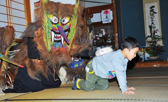 A Raiho-shin known as Toshidon places mochi, a rice cake, on the back of a young boy to grant him good luck.