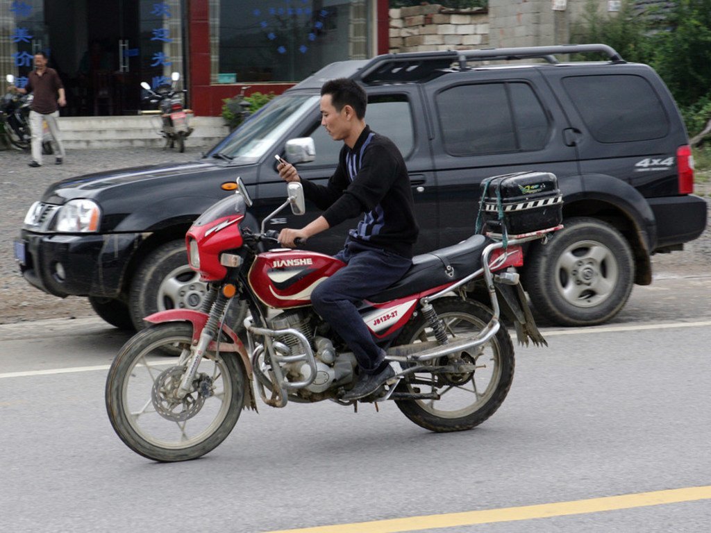在中国，这个人边骑摩托车边看手机。 