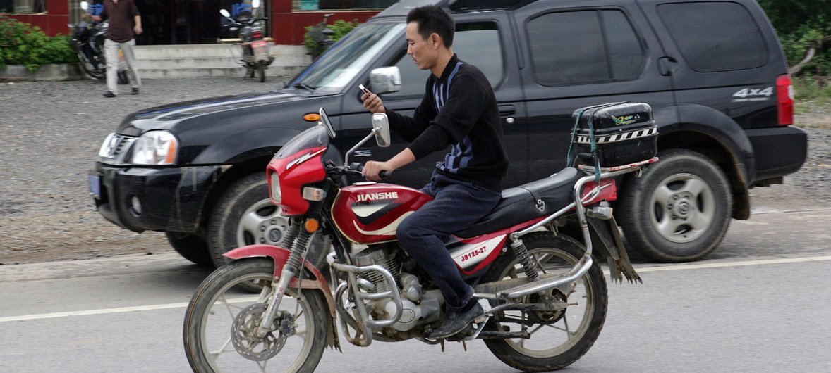 Motorcyclist using a cellphone on the road in China.