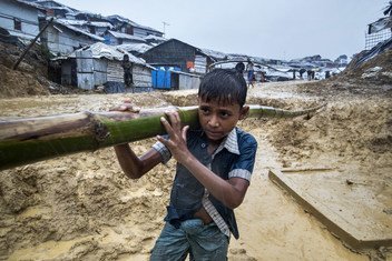 A boy carries bamboo along a very muddy road into the Balukali camp in Cox's Bazar, Bangladesh.  In preparation for the monsoon season, a frenzy of building and reinforcement required vast quantities of bamboo.  13 June 2018.