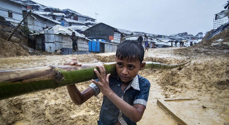 बांग्लादेश के कॉक्स बाज़ार में रोहिंज्या शिविर के पास कीचड़ भरी सड़क पर बांस ले जाता बच्चा. 