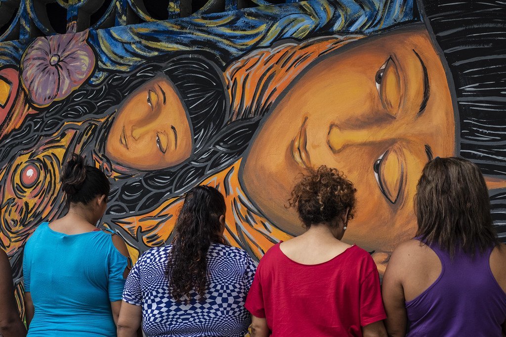 Cuatro mujeres observan un colorido mural pintado por solicitantes de asilo de Centroamérica en un taller artístico en Tapachula, México.