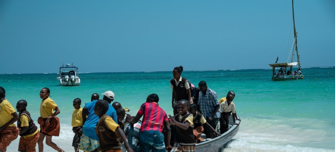 Estudantes nas margens do oceano enquanto aguardam para receber o veleiro de plástico Flipfloppi que fez várias paradas na costa do Quênia