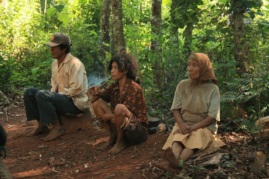 Tres personas de la etnia Mbya Guaraní están sentadas en el suelo en un claro del bosque en Paraguay.