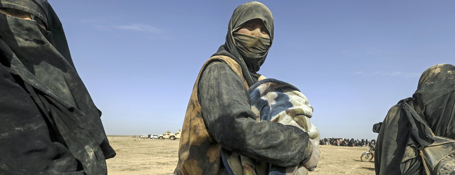 Pessoas deslocadas, incluindo mulheres de niqab, se aglomeram em uma paisagem desértica na vila de Baghoz, distrito de Hajin, zona rural a leste de Deir-ez-Zor, na Síria, antes de sua jornada para o campo de Al-Hol.