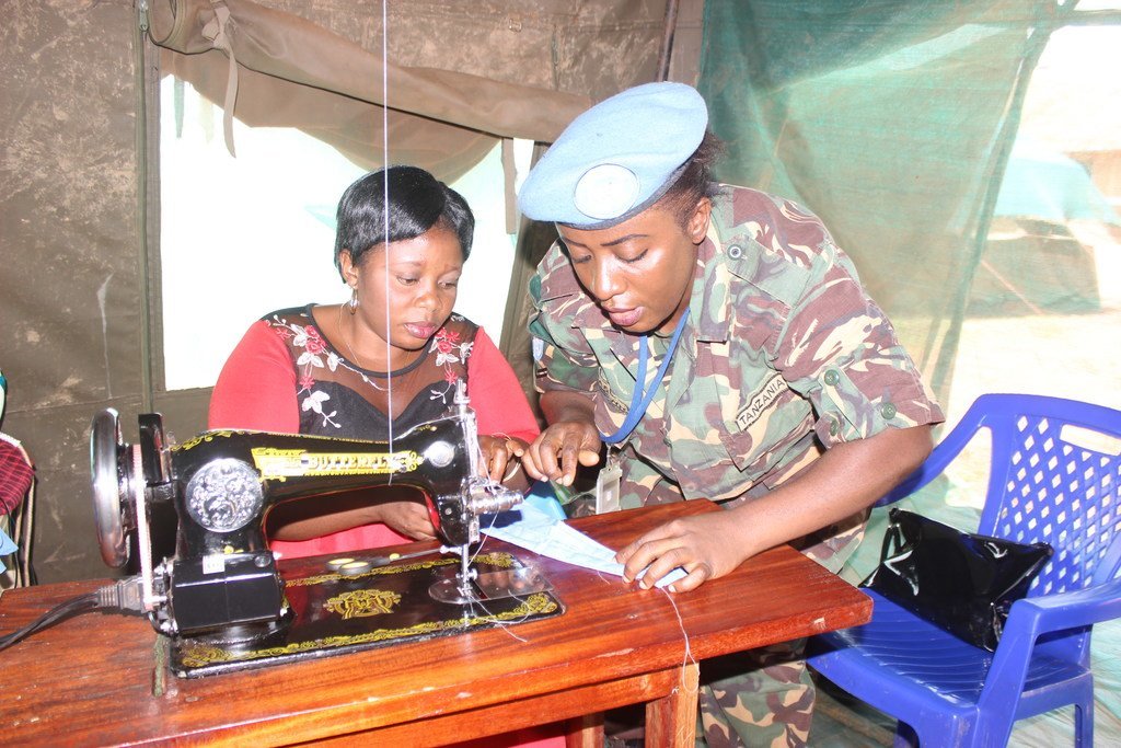 Mlinda amani mwanamke kutoka kikosi cha FIB cha Tanzania cha MONUSCO akimfundisha mwanamke wa eneo hilo kushona kipande cha kitambaa kwa kutumia mashine ya kushona.