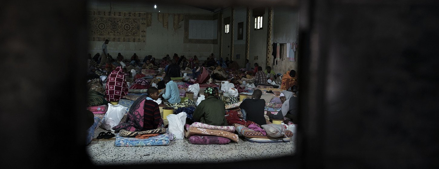 Libya'da bulunan bir gözaltı merkezinde göçmenler yere serilen şilteler üzerinde oturuyor.