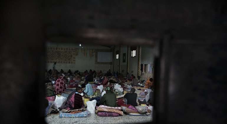 Seen through the aperture of an iron door, migrants sit on mattresses laid on the floor at a detention centre, located in Libya.
