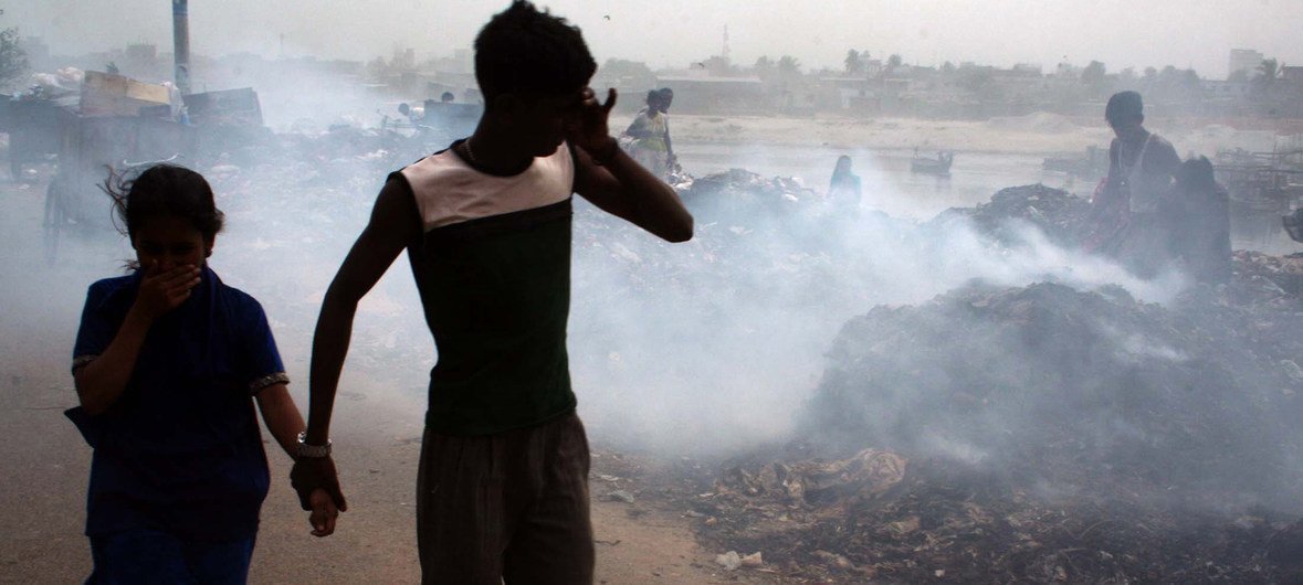 बांग्लादेश की राजधानी ढाका में जलते कूड़े के ढेर के पास से गुज़रते लोग.